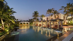 A swimming pool with a tiled edge, surrounded by palm trees and a building with a covered seating area. - Mayfair Palm Beach Resort  (Brahmapur)