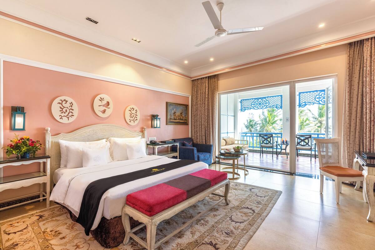 A spacious bedroom with a large bed, a bench, a desk, and a balcony with outdoor furniture.