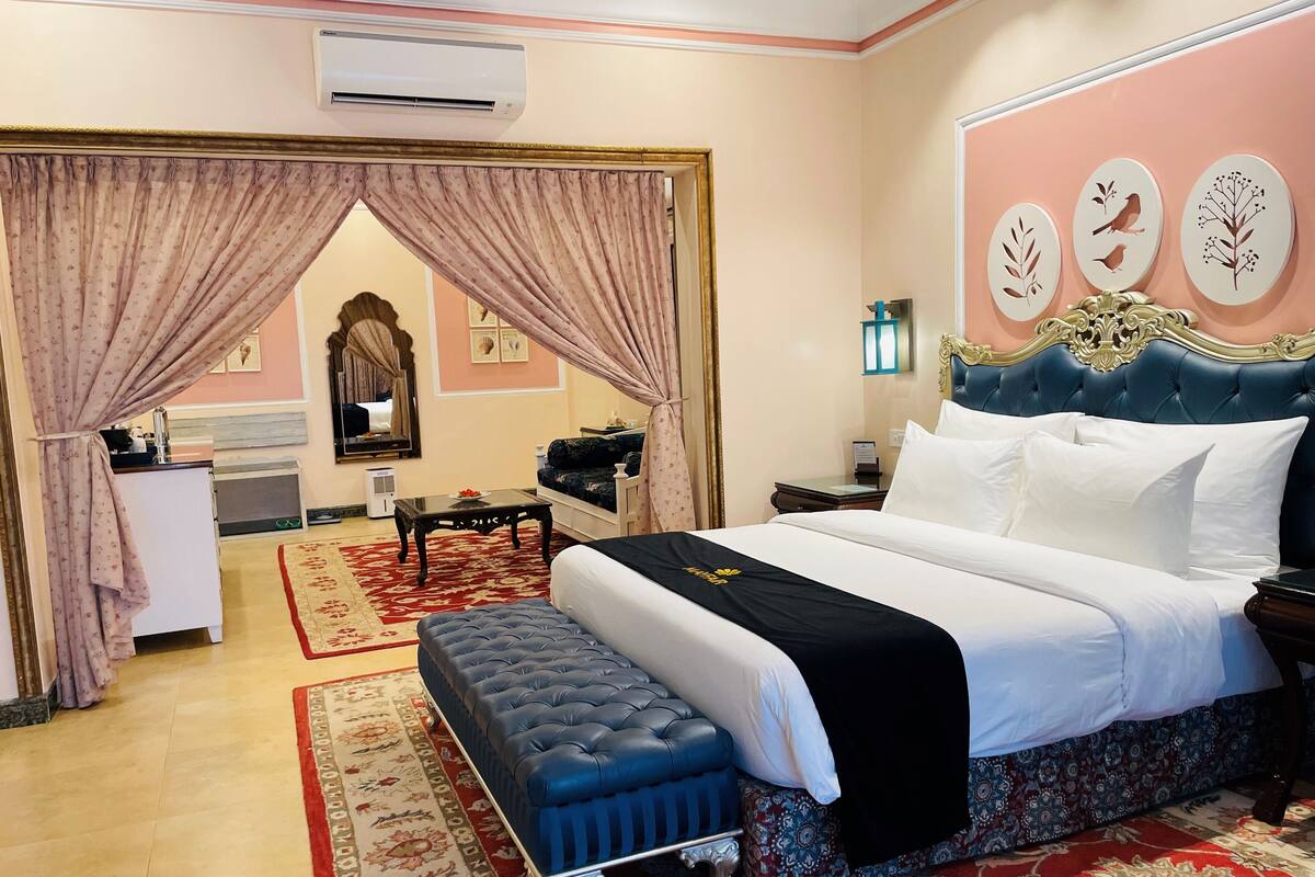 A hotel room with a large bed, a sitting area with a sofa and a table, a mirror, and a red patterned rug.