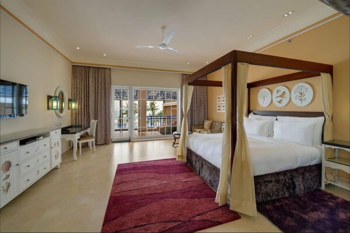 A bedroom with a four-poster bed, a desk with a chair, a TV, and a balcony with a view.