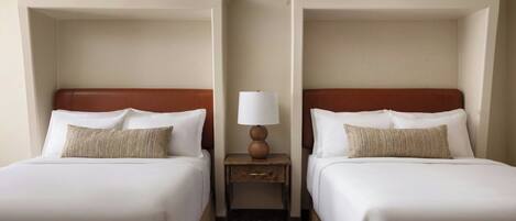 A hotel room with two beds, a nightstand with a lamp, and a patterned carpet.