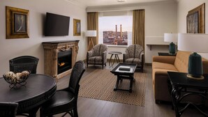 A hotel room with a fireplace, a television, two armchairs, a sofa, a coffee table, and a view of the cityscape. - The Davenport Tower, Autograph Collection (Spokane)