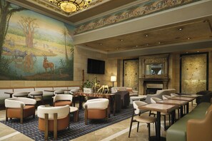 A spacious lobby with a large mural of wildlife, comfortable seating, a fireplace, and a television mounted on the wall. - The Davenport Tower, Autograph Collection (Spokane)