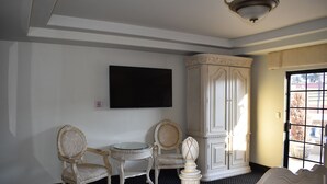 A room with a bed, two chairs, a small table, a cabinet, and a television on the wall.