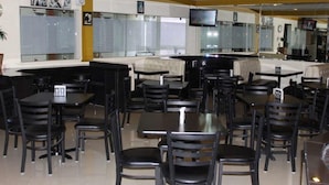 A restaurant with multiple tables and chairs, a television mounted on the wall, and a window with blinds.