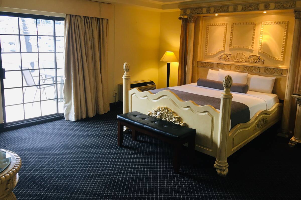 A hotel room with a large bed, a bench, a desk, and a view of the outside.