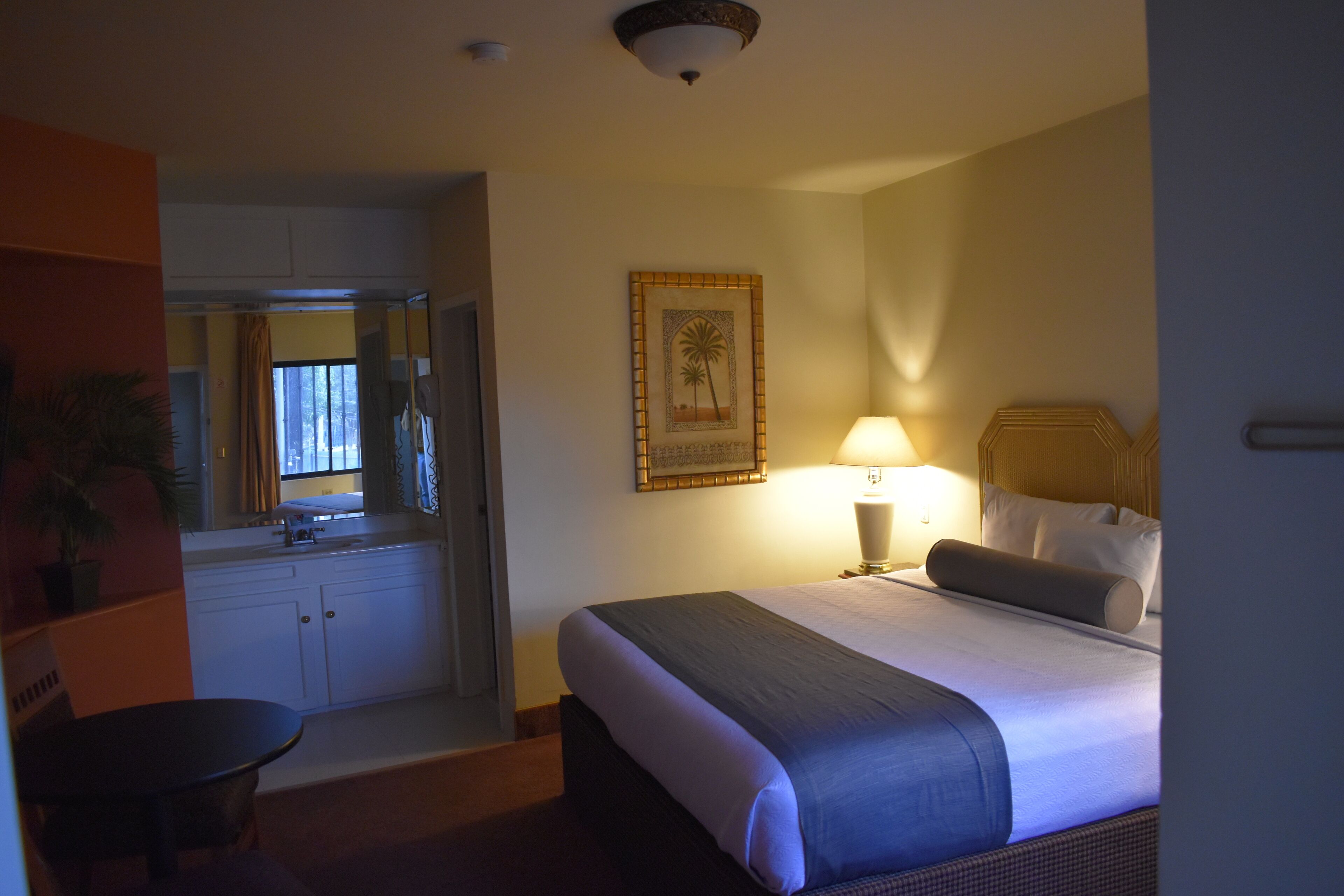 Habitación de hotel con cama, lámpara de noche y un cuadro en la pared.