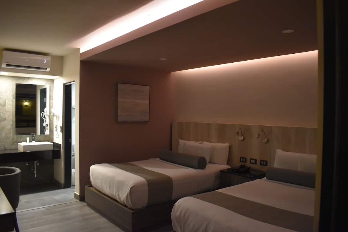 A hotel room with two beds, a bathroom, and a nightstand with a phone.