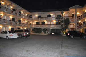 Un hotel de varios pisos con un patio central, que cuenta con un estacionamiento con varios automóviles, una escalera y un exterior bien iluminado.