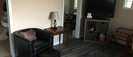 A living room with a black leather chair, a small table with a lamp, a television on a stand, and a wooden cabinet.