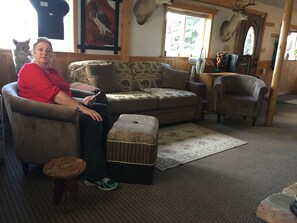 A cozy living room with a sofa, ottoman, and armchair, a small table, and a window with a view. - Big Bear Lodge (Alpena)