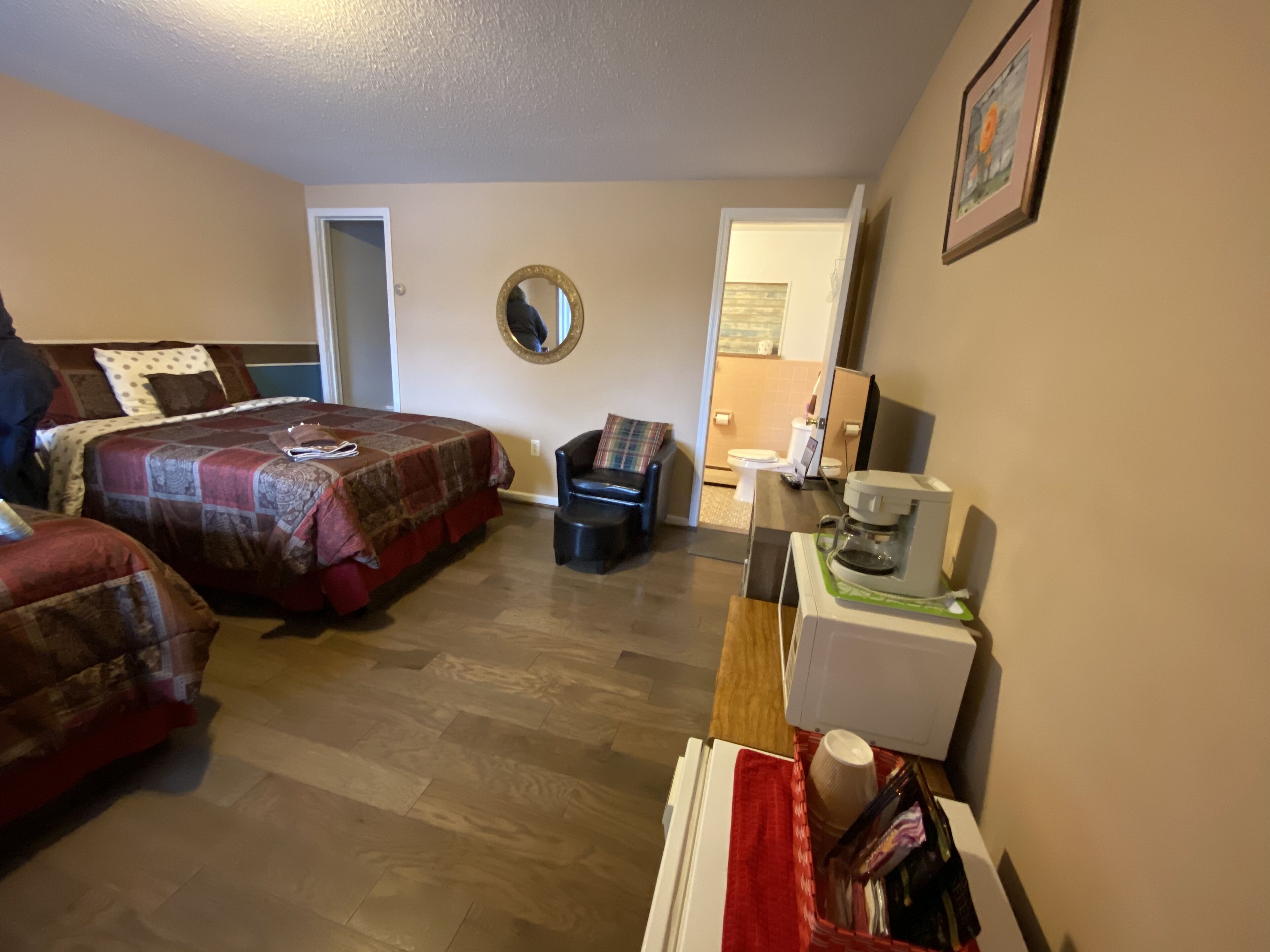 A bedroom with two beds, a coffee maker, a chair, and a bathroom visible through an open door.