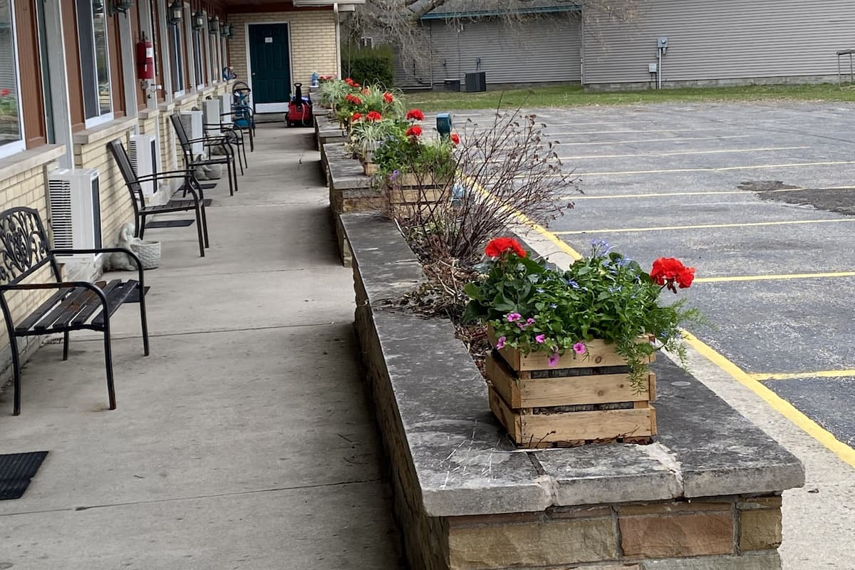 A motel with a row of flower planters along the walkway, outdoor seating, and a parking lot.