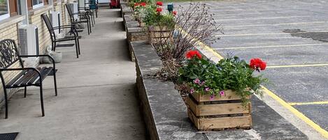 A motel with a row of flower planters along the walkway, outdoor seating, and a parking lot.