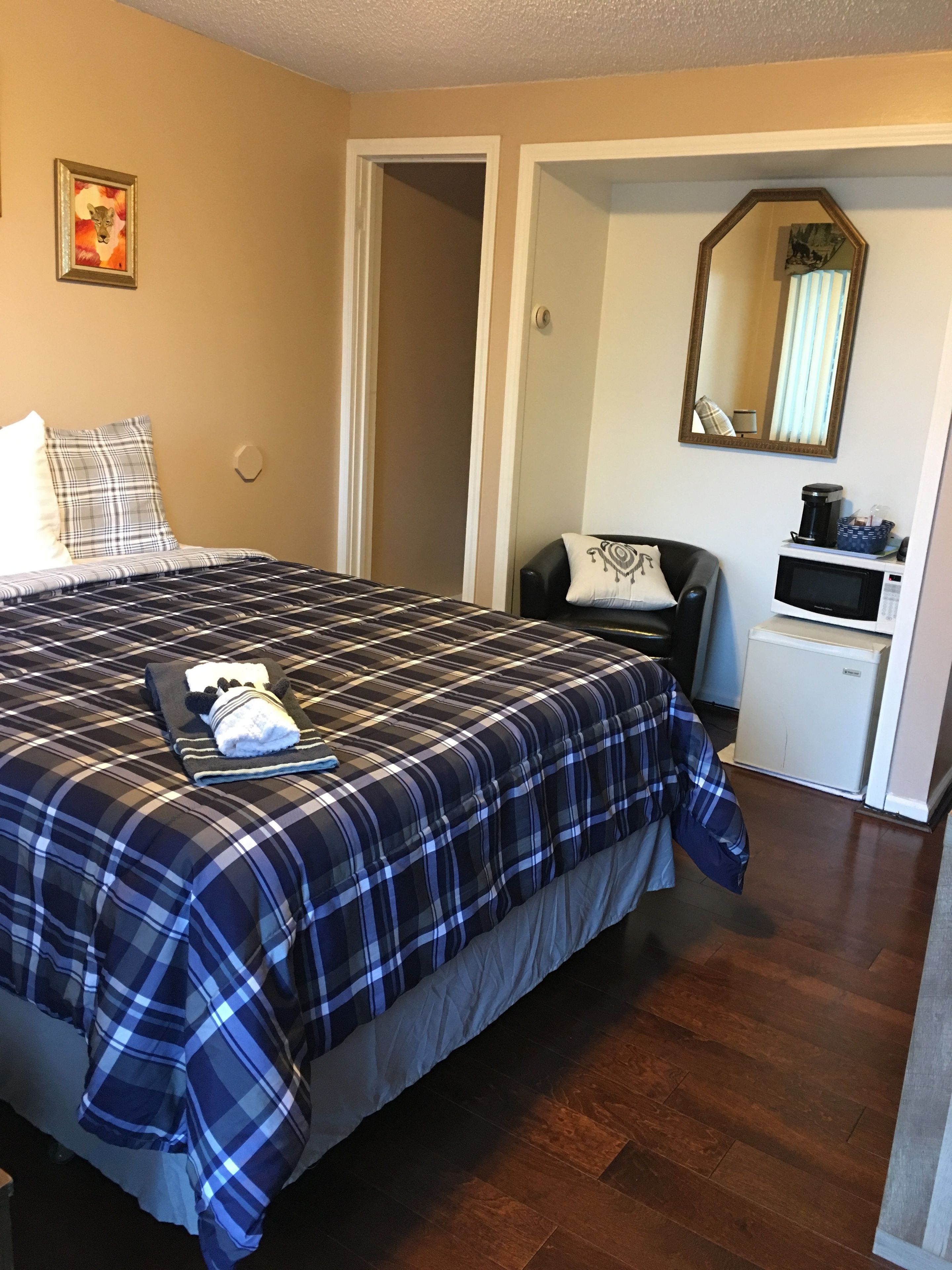 A bedroom with a large bed, a chair, a microwave, and a small refrigerator.