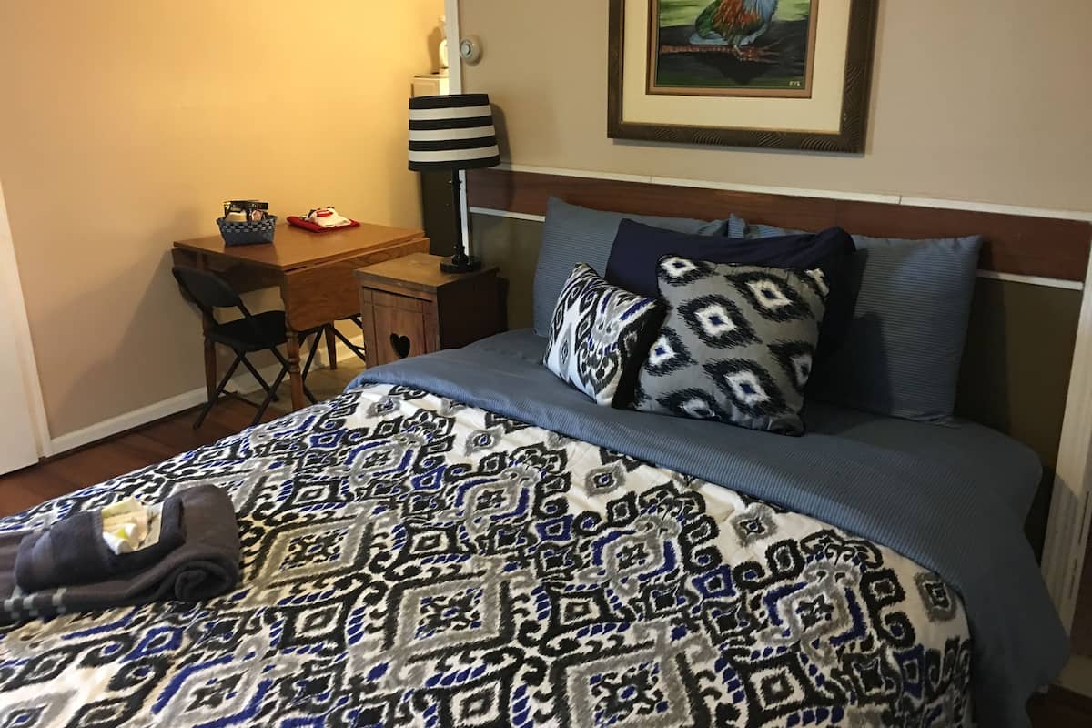 A neatly made bed with patterned bedding, a desk with a lamp, and a framed picture on the wall.