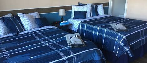 A hotel room with two beds, each with blue and white striped bedding, a nightstand with a lamp, and a painting on the wall.