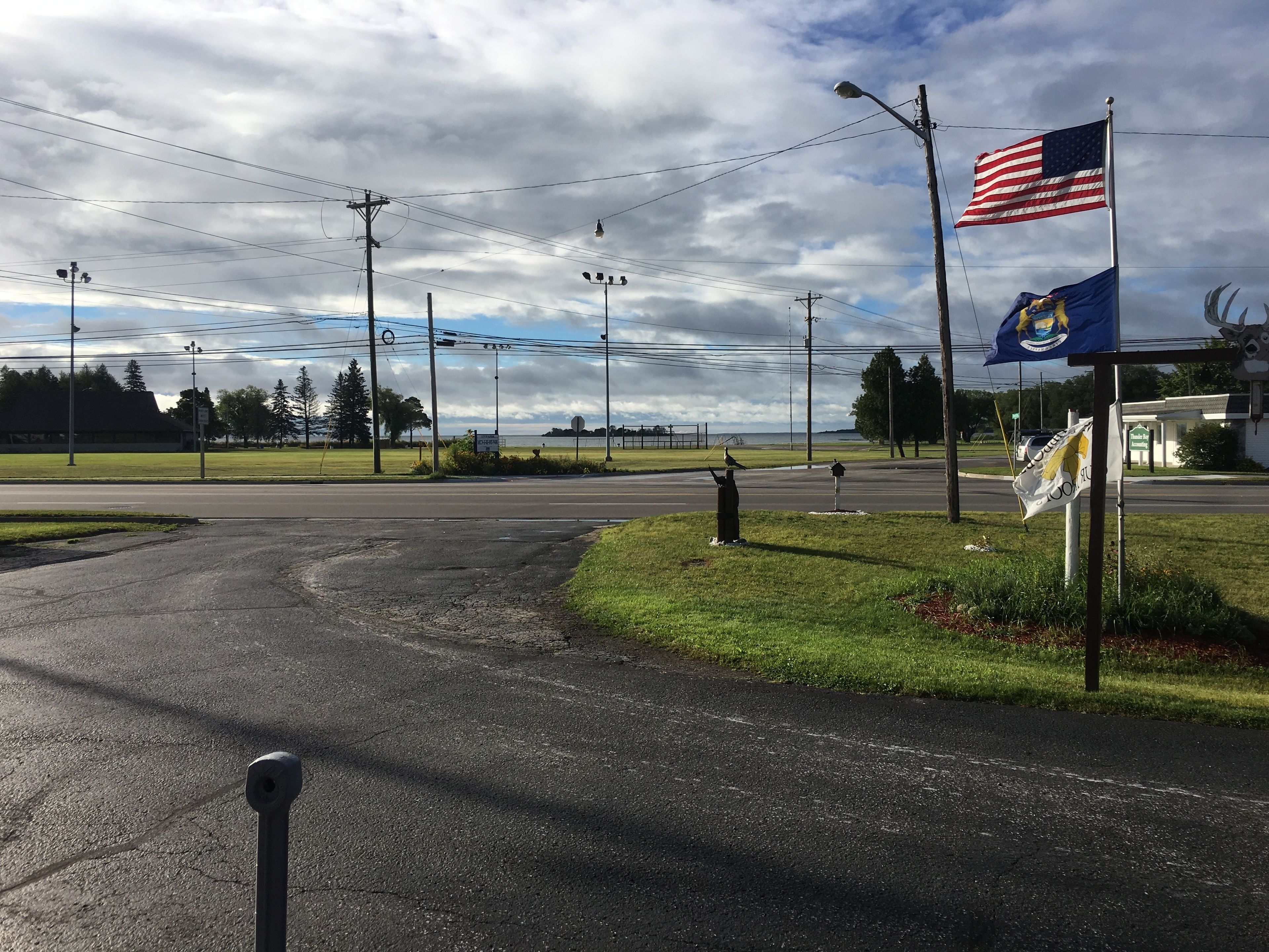 A road intersection with a grassy area, a street lamp, and a flagpole with an American flag and a state flag.