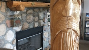 A stone wall with a fireplace, a mounted television, and a wooden sculpture. - Big Bear Lodge (Alpena)