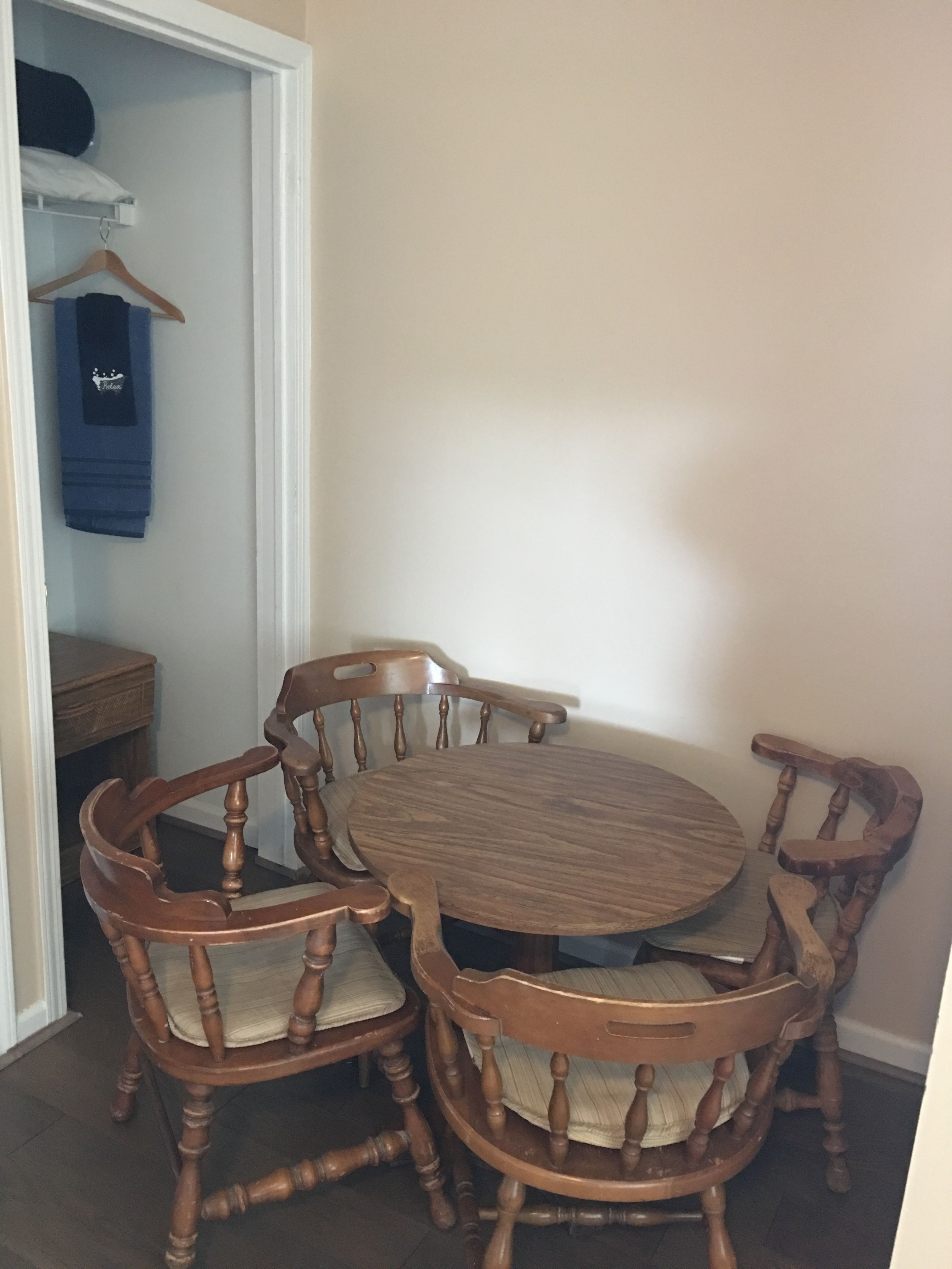 Un coin repas comprenant une table ronde en bois et quatre chaises, un banc en bois, ainsi qu’une petite table en bois sur laquelle est posé un vêtement bleu suspendu.