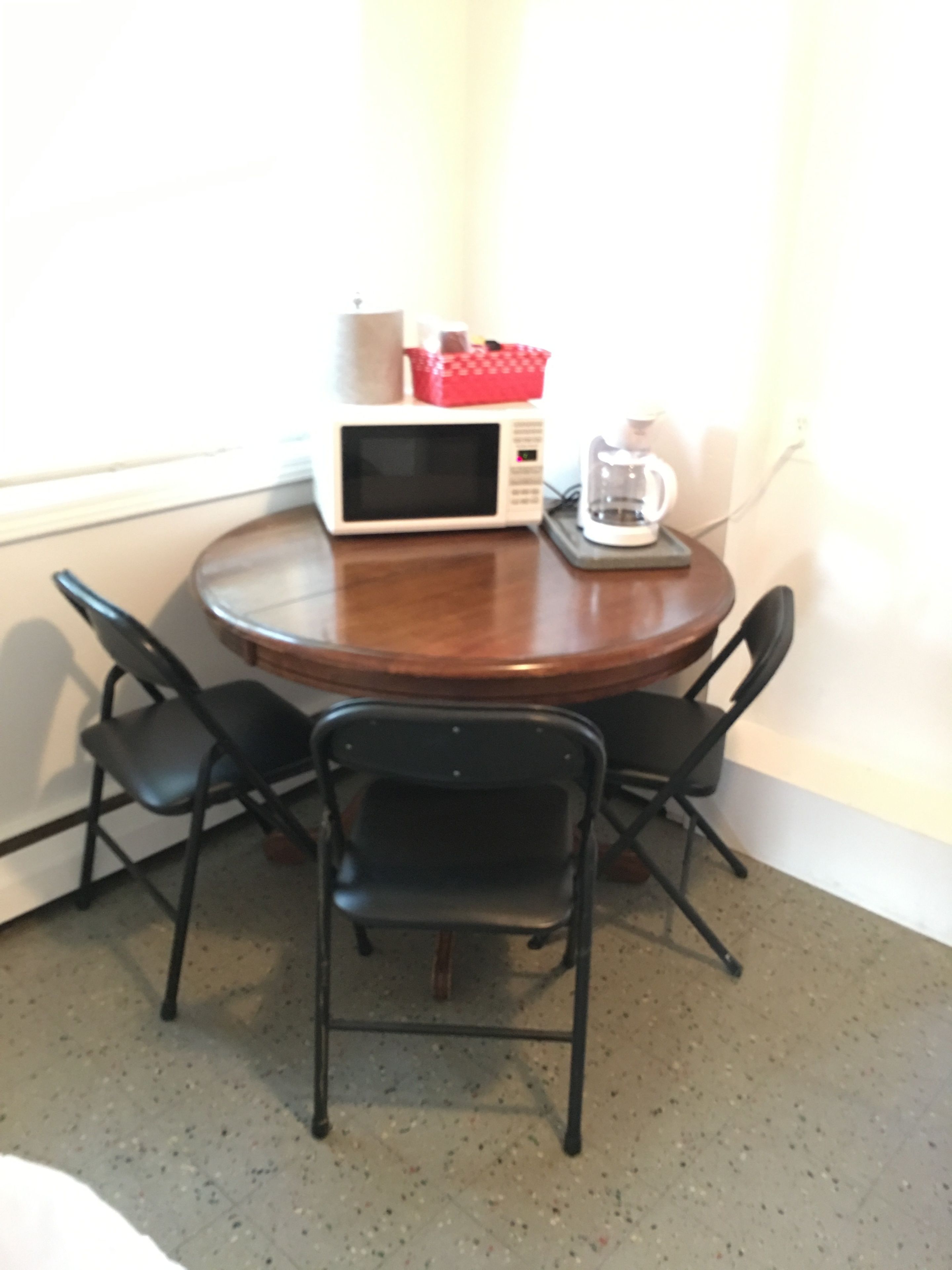 A small dining area with a round table, two black chairs, a white microwave, and a coffee maker.
