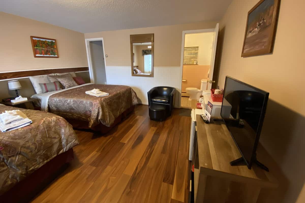 A hotel room with two beds, a desk with a television, a mirror, and a door leading to a bathroom.