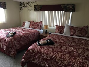 A hotel room with two beds, each with red and white patterned bedding, a nightstand with a lamp, and a wall-mounted artwork. - Big Bear Lodge (Alpena)