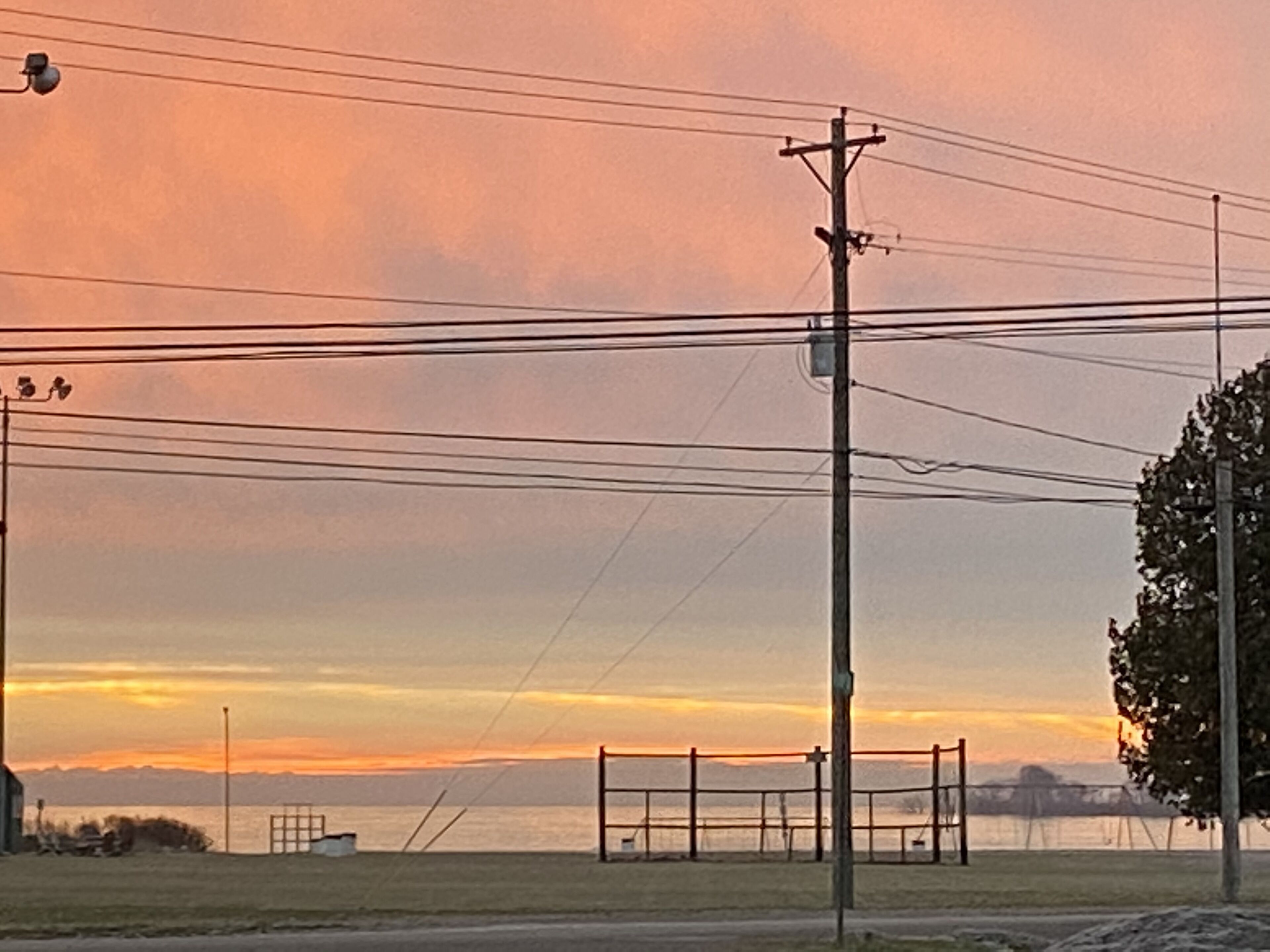 A sunset view with a fence, utility pole, and a body of water.