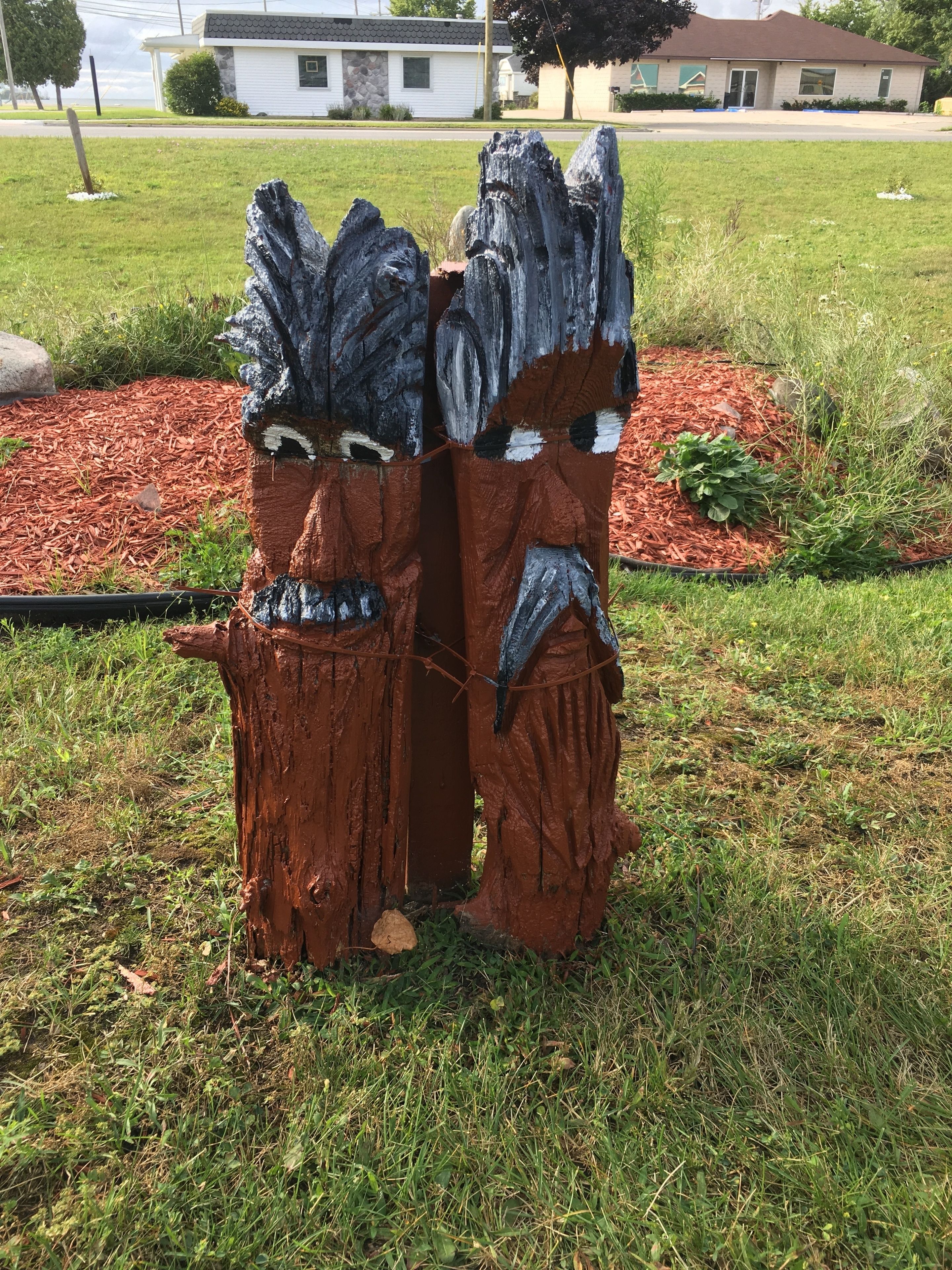 Una escultura de madera en un área con césped, con un edificio al fondo.