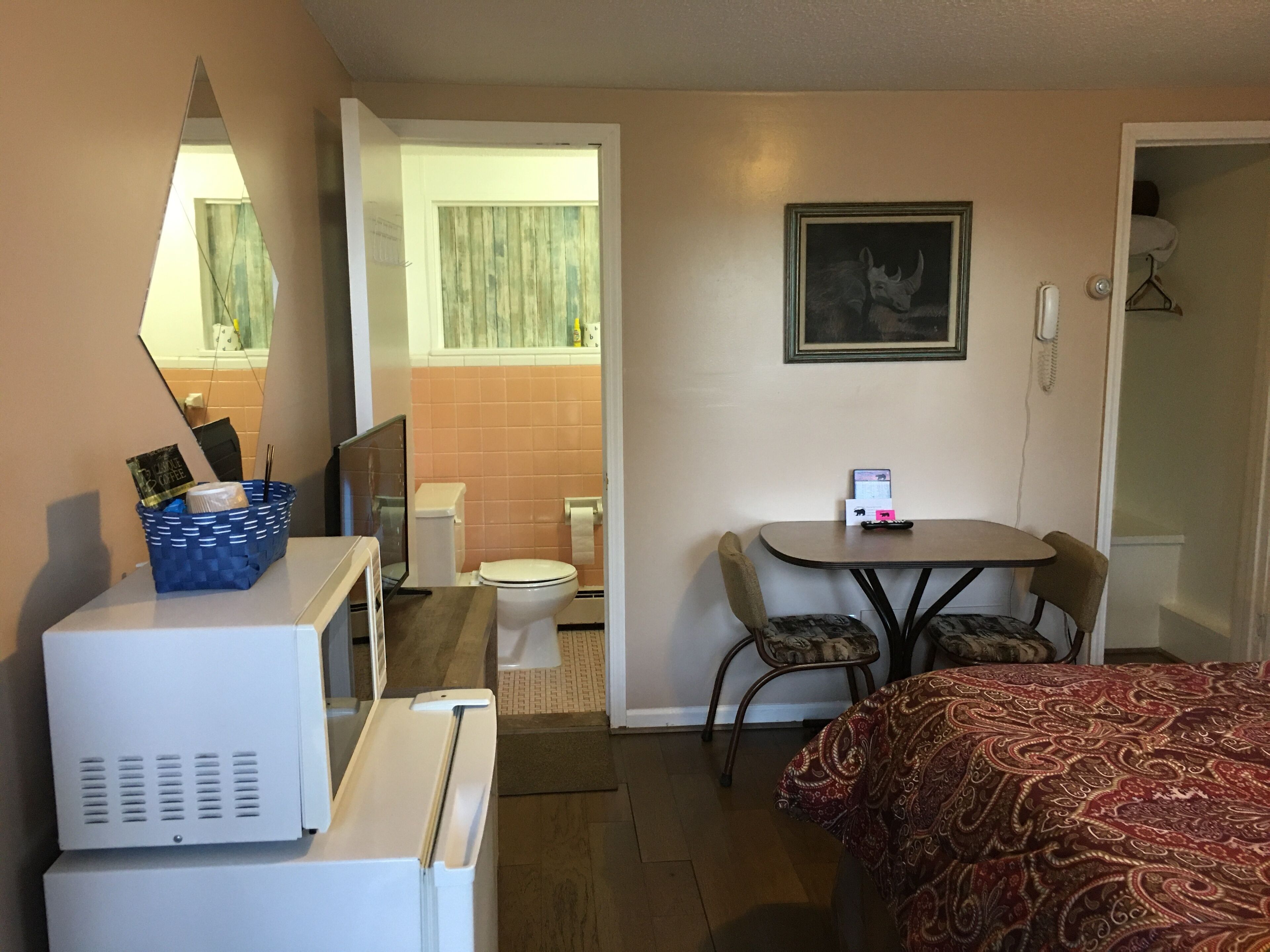 A hotel room with a bed, a desk with a chair, a microwave, a refrigerator, a bathroom with a toilet and sink, and a framed picture on the wall.
