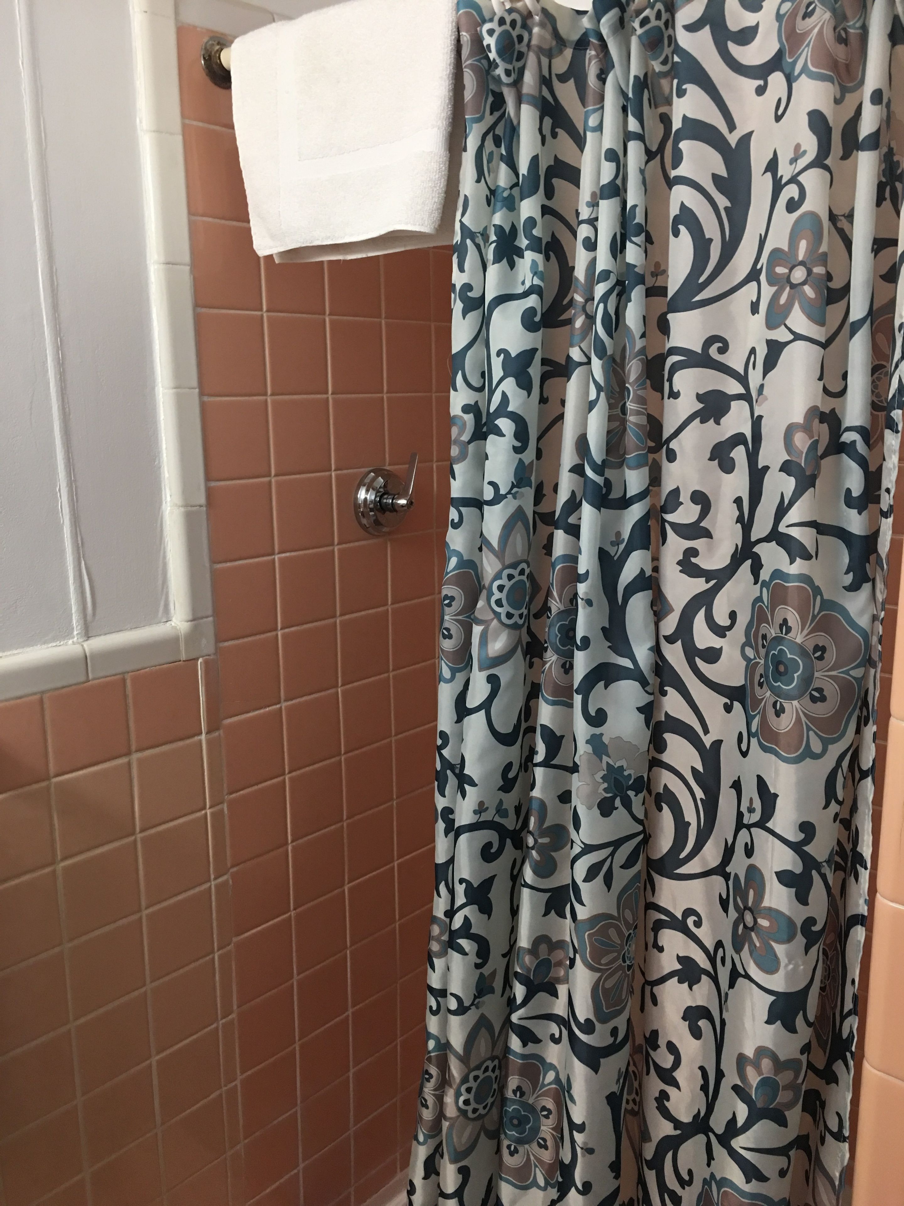 A bathroom with a shower curtain featuring a floral pattern, a white towel hanging on a rack, and a door with a silver handle.