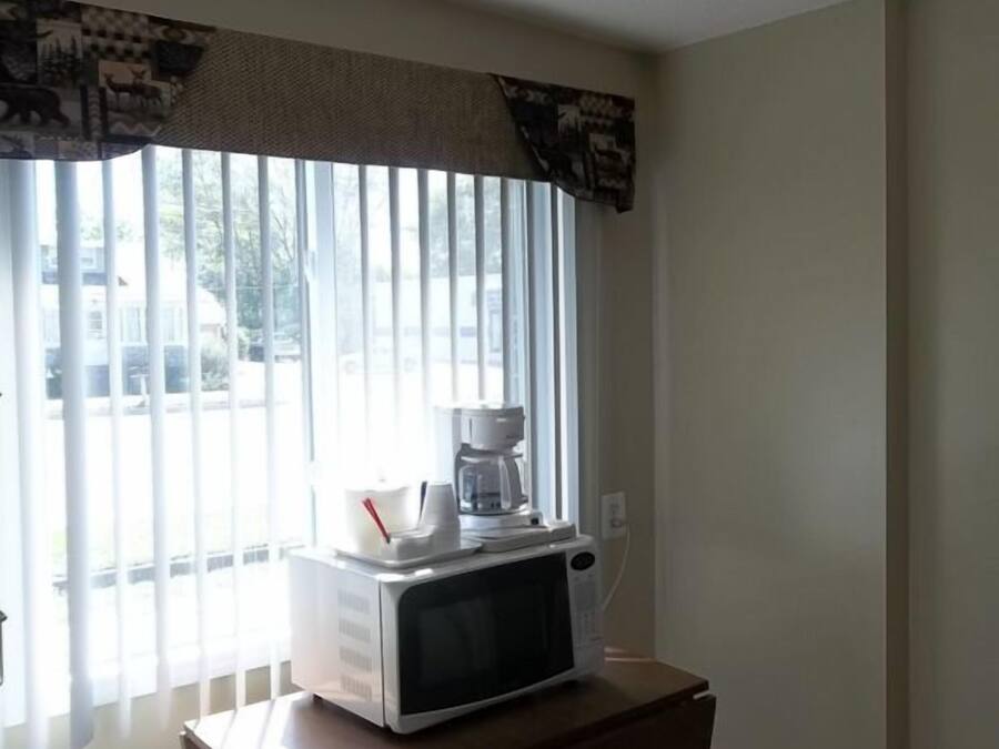 Une cuisine avec un four à micro-ondes posé sur une table en bois, une fenêtre avec des stores et une vue sur l’extérieur.