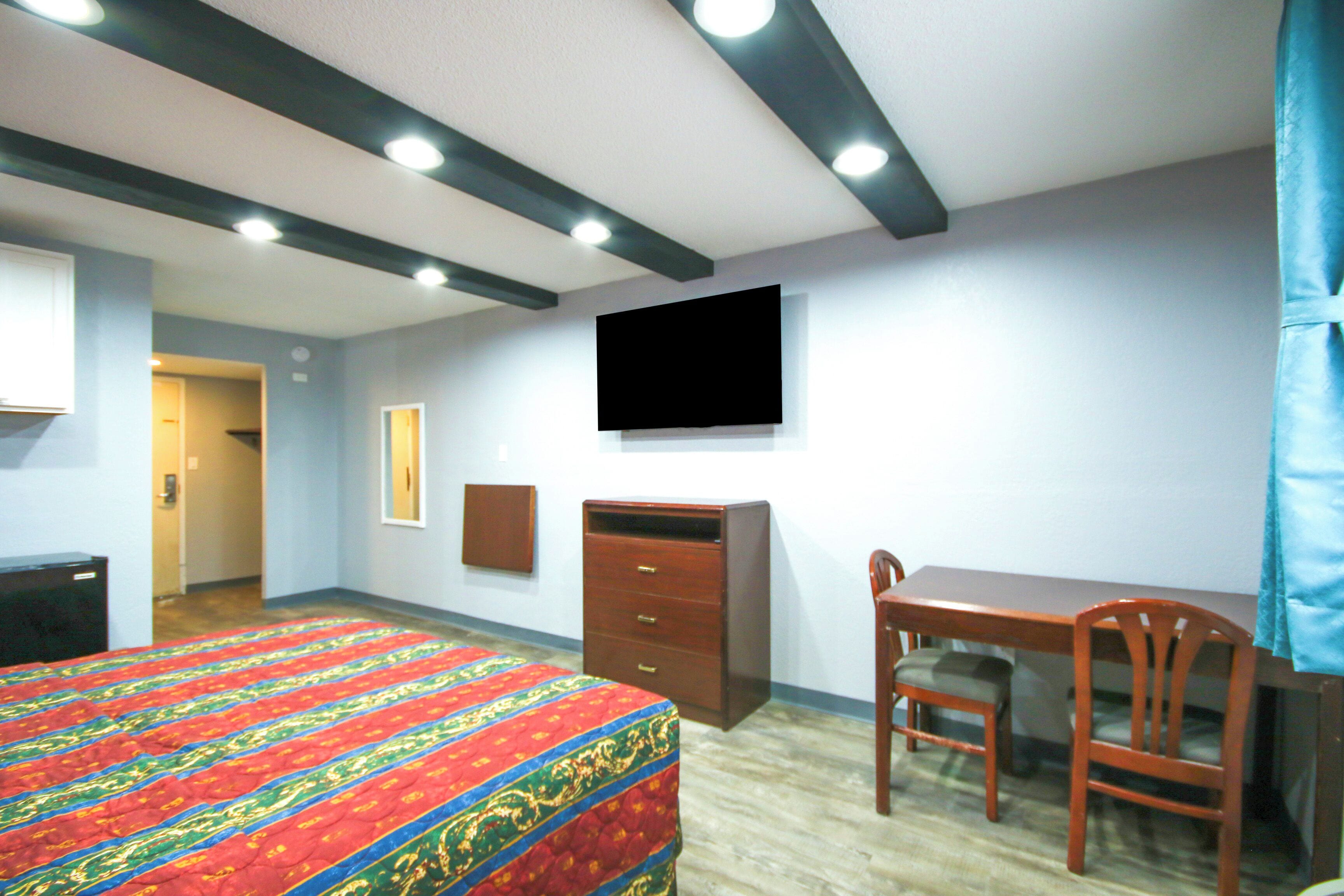 Habitación de hotel con cama, escritorio, silla, televisor montado en la pared y armario.