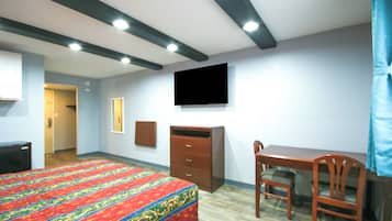 Habitación de hotel con cama, escritorio, silla, televisor montado en la pared y armario.