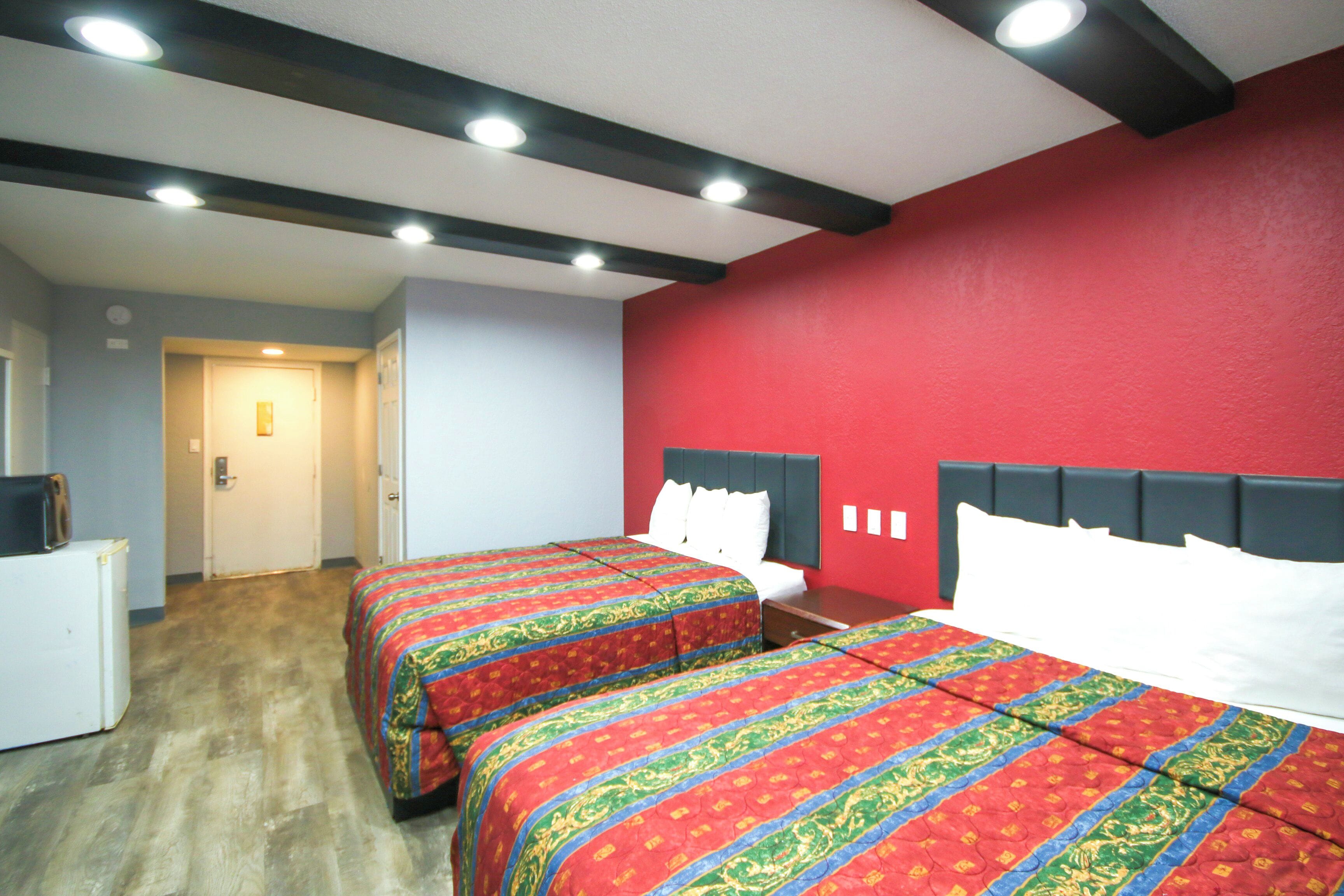 Habitación de hotel con dos camas, una pared de acento roja y suelo de madera.