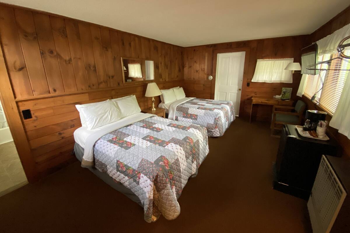 A room with two beds, wooden walls, a desk, and a chair.