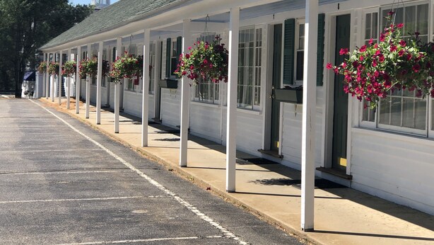 A row of white buildings with green shutters, each with hanging flower baskets. - School House Inn (North Conway)
