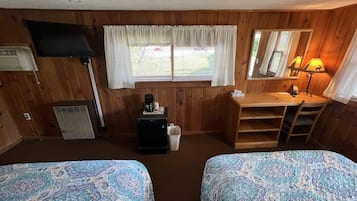Ein Zimmer mit zwei Betten, einem Schreibtisch, einer Lampe und einem Fenster mit Jalousien.