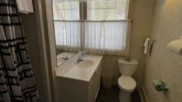 Une petite salle de bain comprenant un lavabo, des toilettes et une fenêtre équipée de stores.