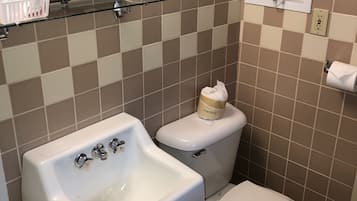 A bathroom with a sink, toilet, and a mirror. There is a towel rack above the toilet and a soap dispenser on the sink.