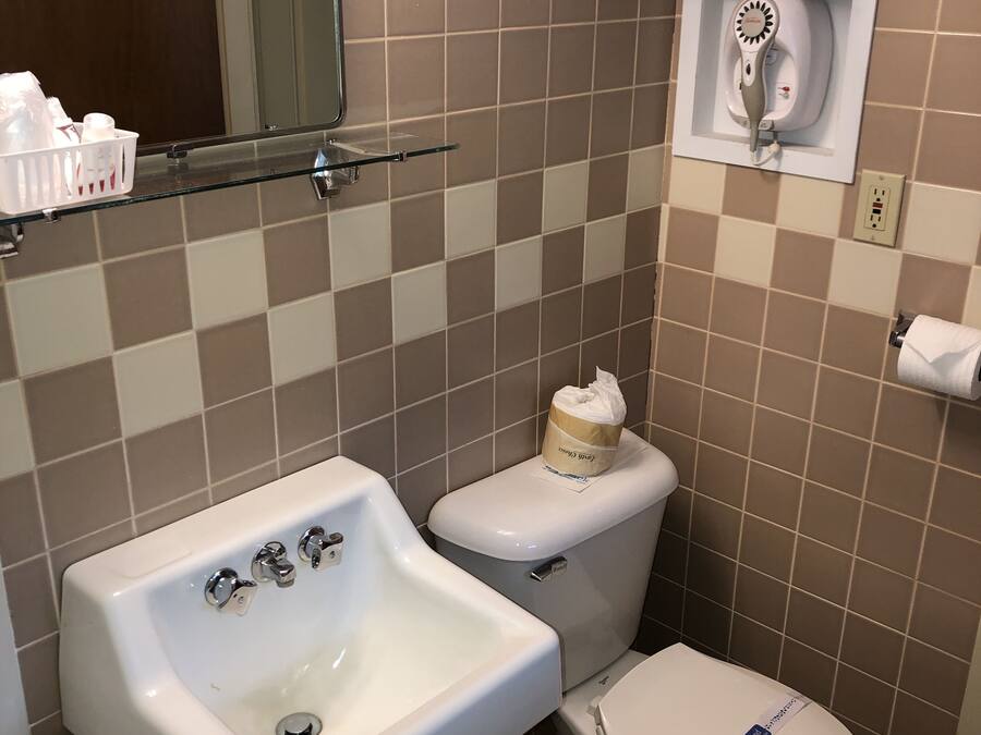 A bathroom with a sink, toilet, and a mirror. There is a towel rack above the toilet and a soap dispenser on the sink.