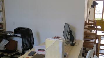 Una habitación con escritorio, computadora, silla y ventana con persianas.