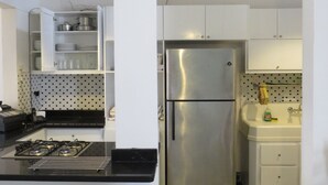 Eine Küche mit Gaskochfeld, Edelstahlkühlschrank, weißen Schränken und einem karierten Boden.