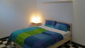 Ein kleines, ordentlich eingerichtetes Schlafzimmer mit einem Bett, einem Nachttisch und einem an der Wand befestigten Regal.