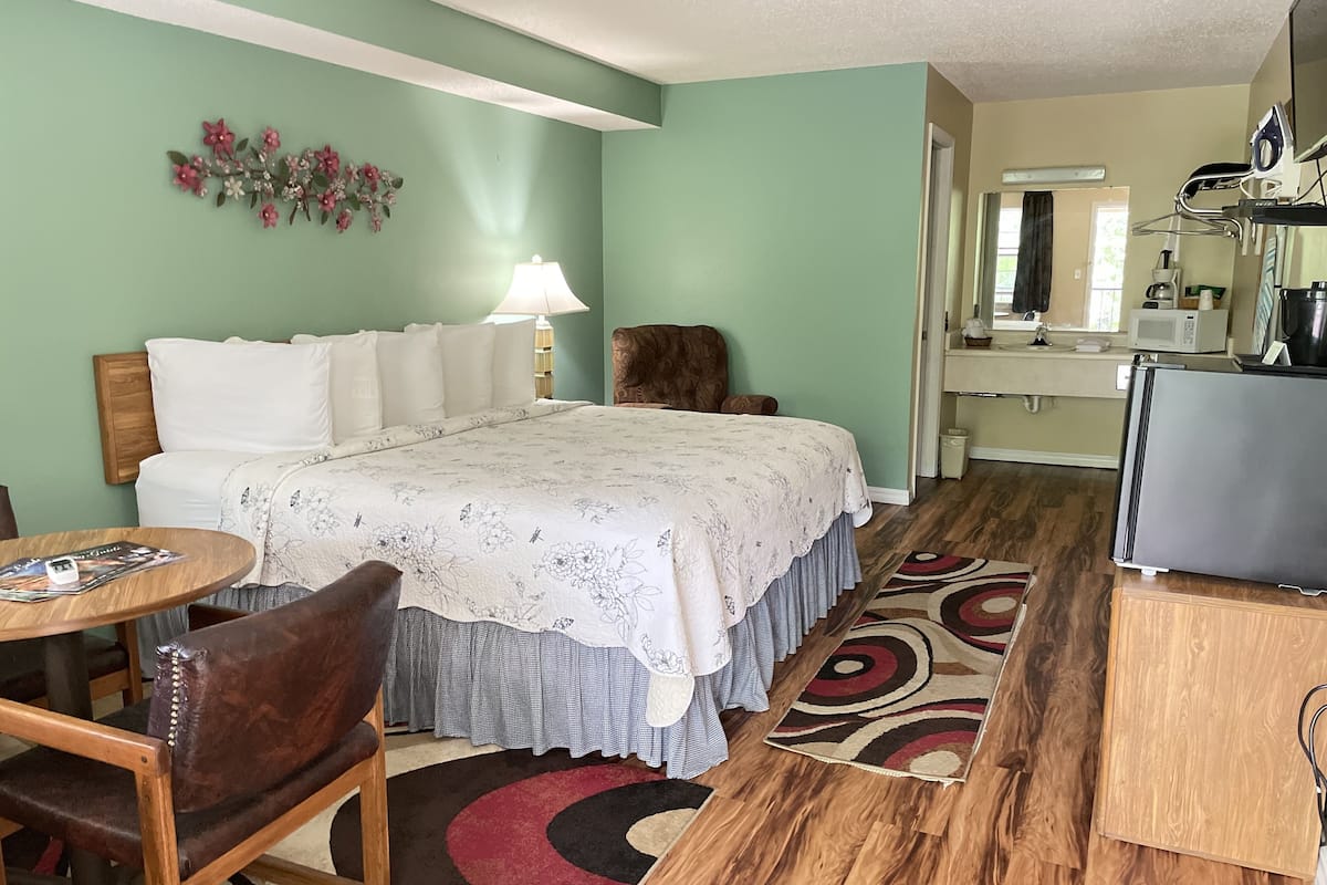 A bedroom with a bed, a desk, a chair, a lamp, and a small table.