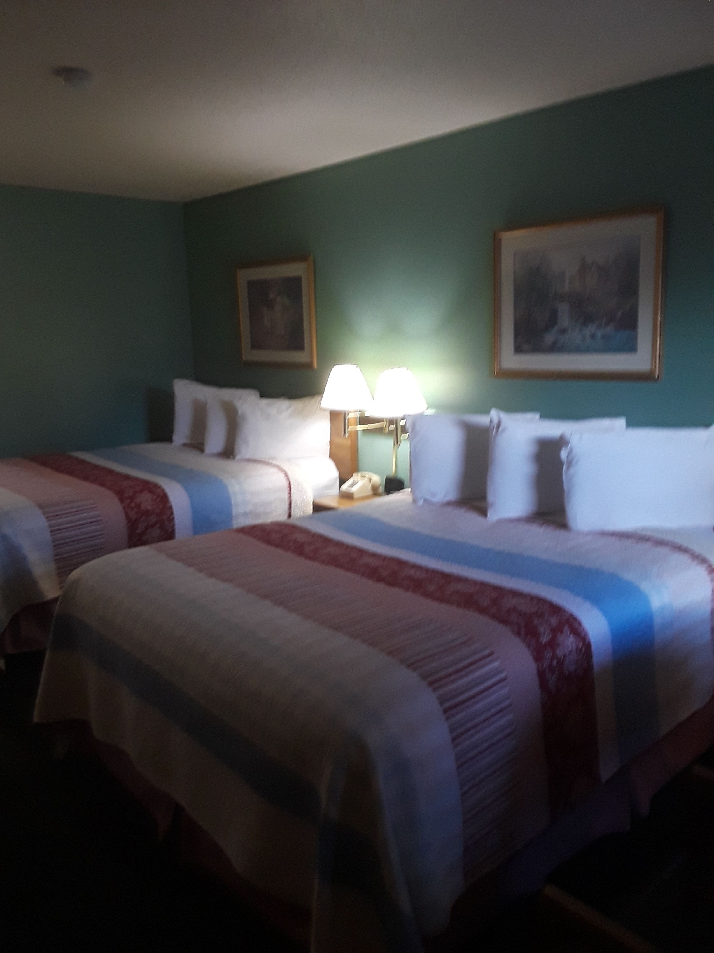 Ein Hotelzimmer mit zwei Betten, einem Nachttisch, einer Lampe und zwei gerahmten Bildern an der Wand.