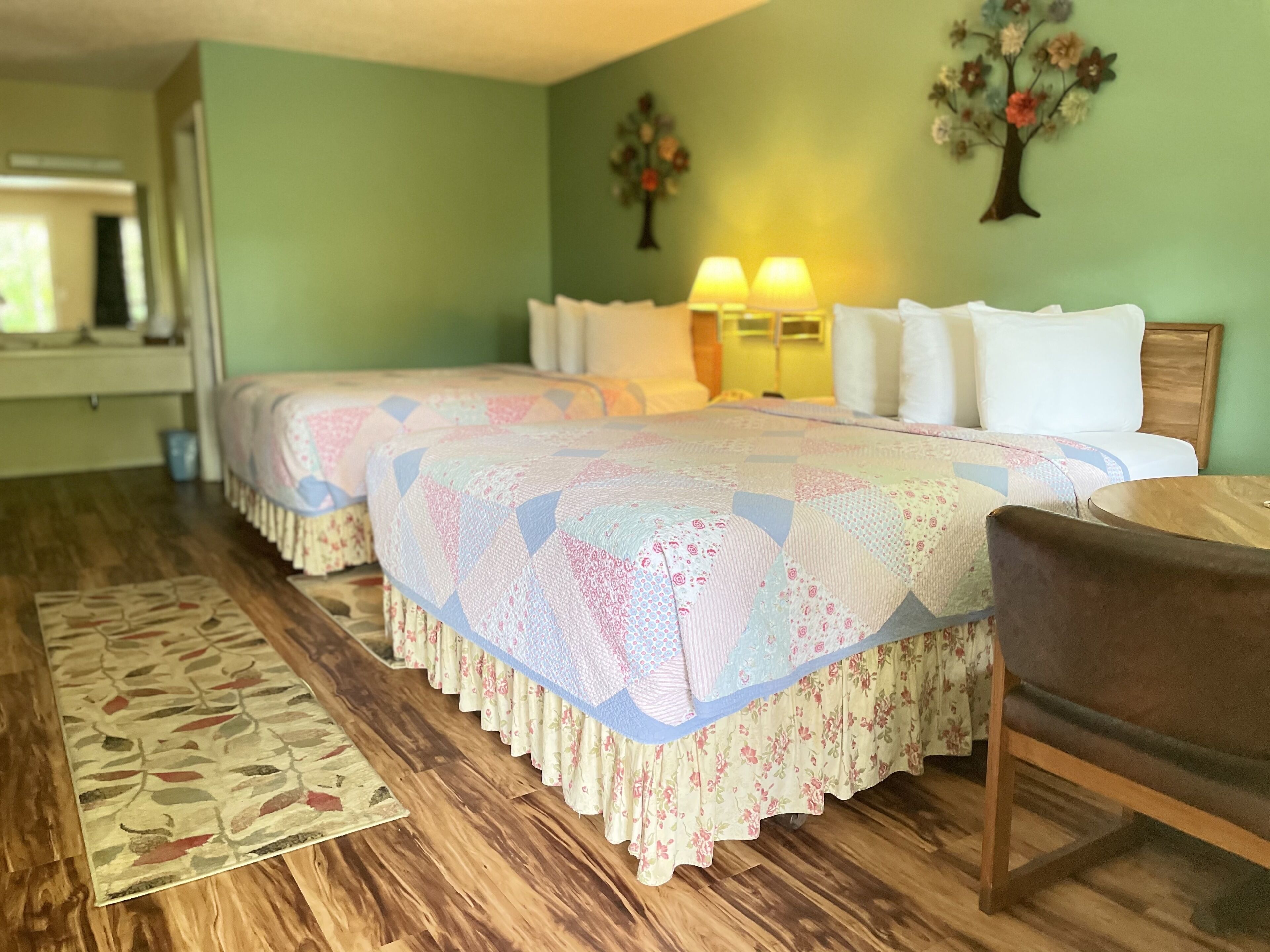 Une chambre avec deux lits, un plancher en bois, un tapis à motifs floraux et une table de chevet avec des lampes.