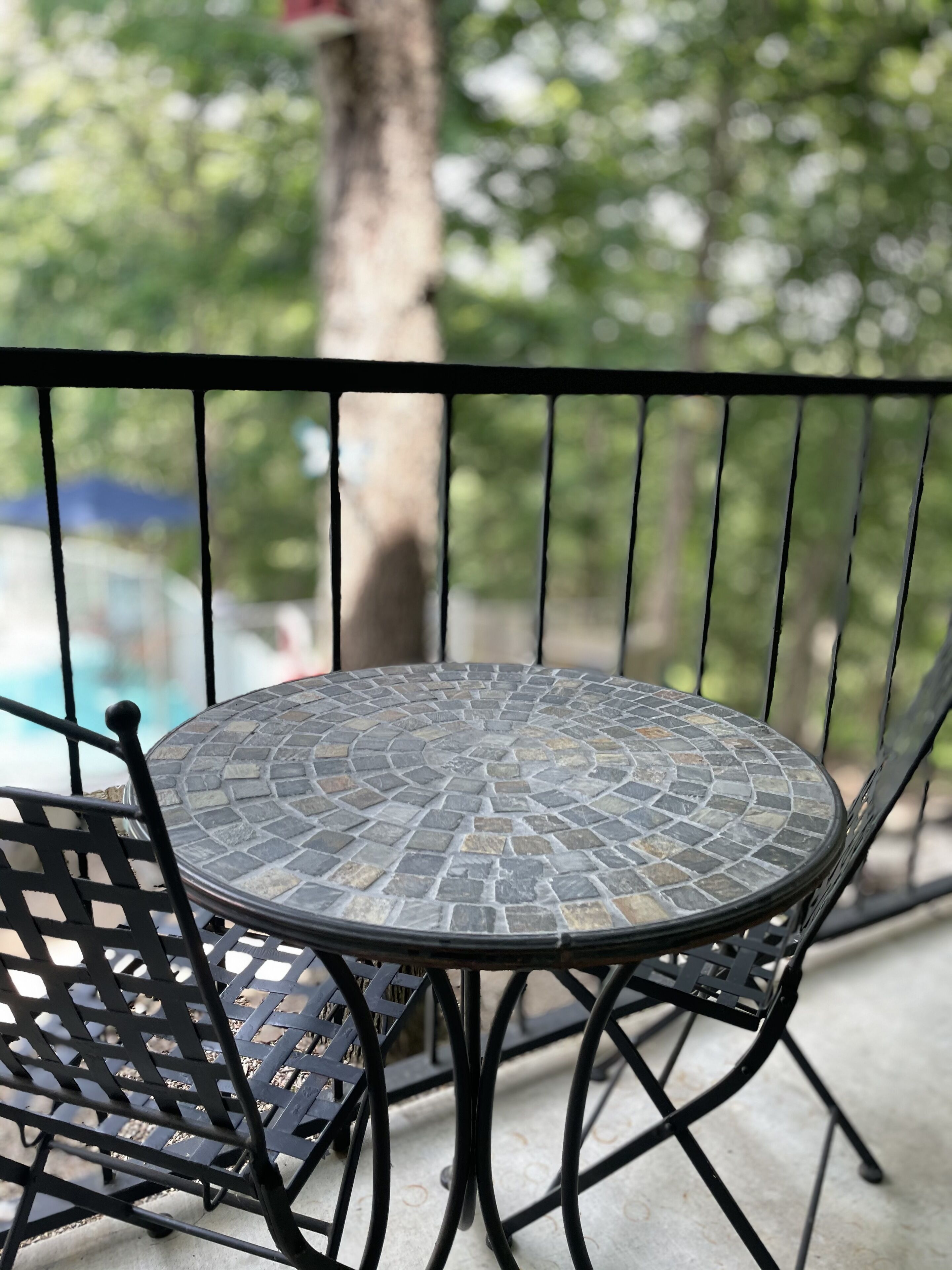 Une table ronde d’extérieur, dotée d’un plateau en mosaïque, entourée d’une chaise en métal noir avec un dossier ajouré.
