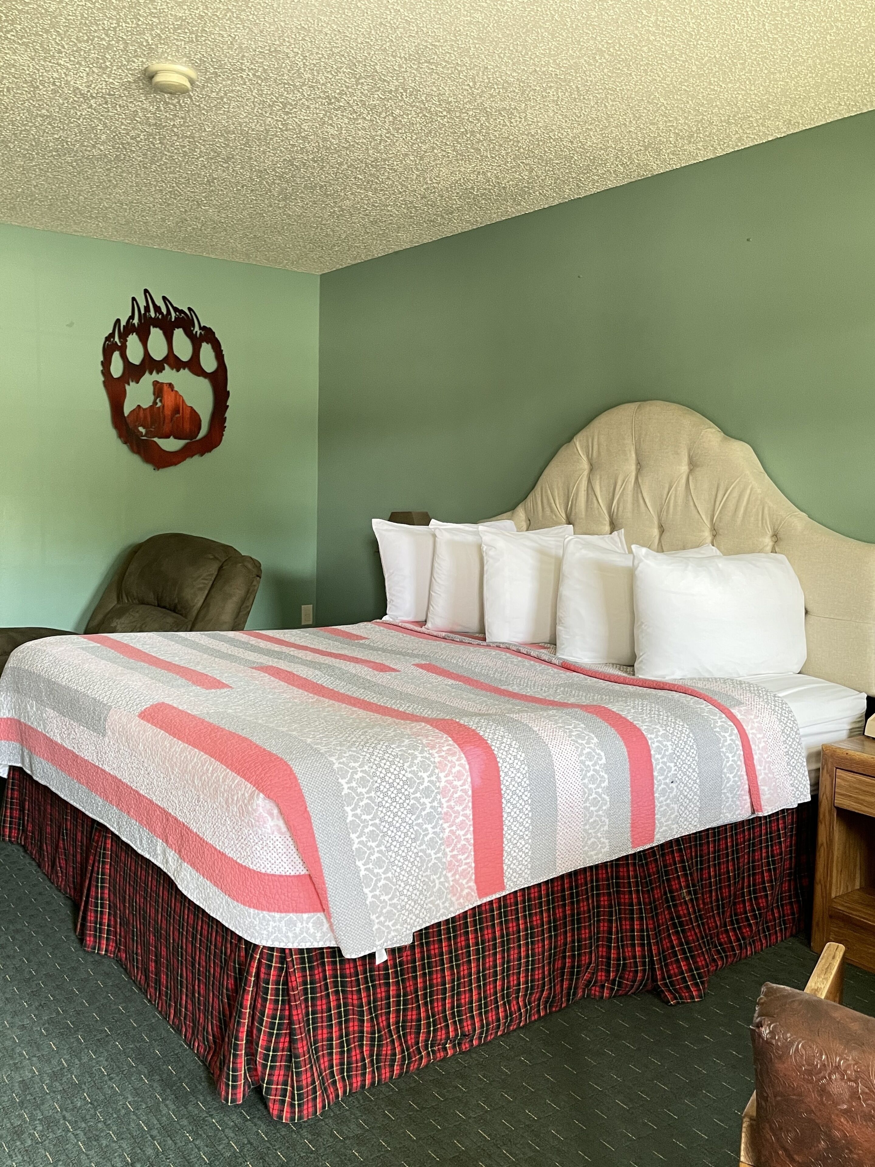 A bedroom with a bed, a chair, a wall decoration, and a wooden nightstand.