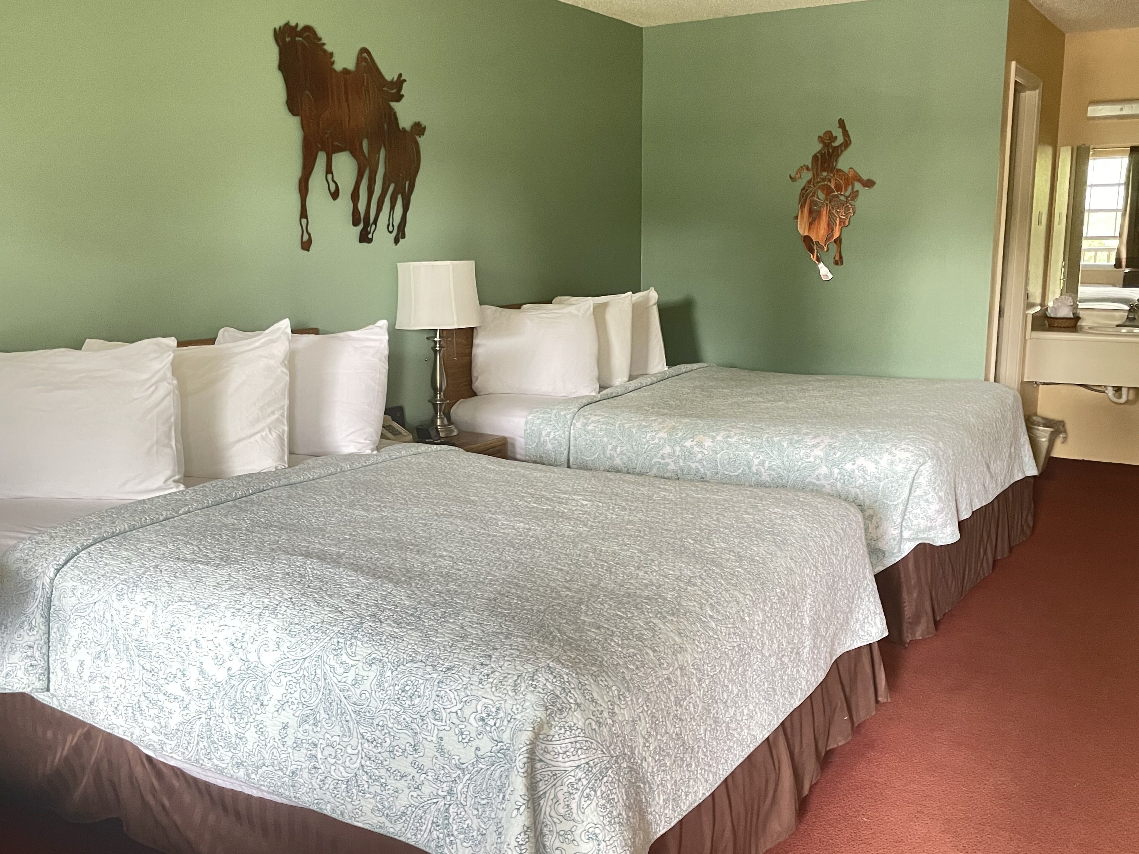 A hotel room with two beds, a lamp, and wall art of a horse and a cowboy.